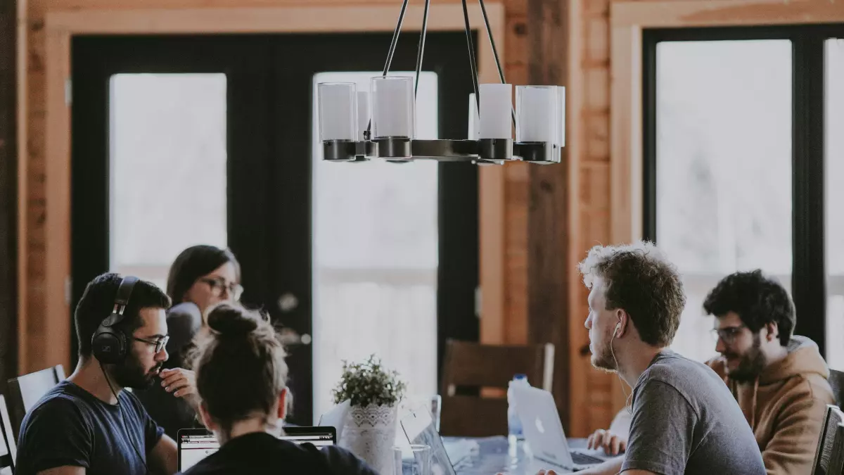 A group of young professionals collaborating around a large wooden table with laptops.