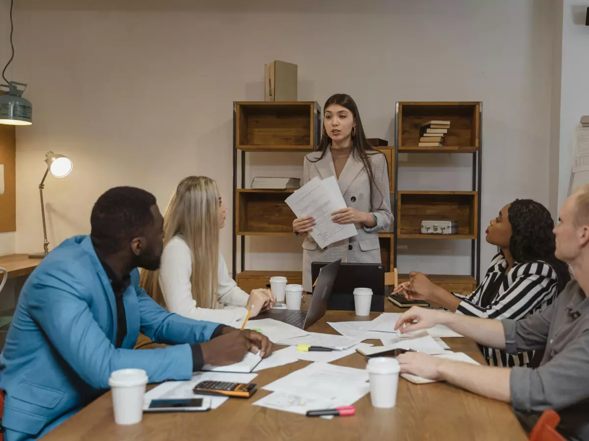 A woman in a meeting room speaking in front of a group of people.