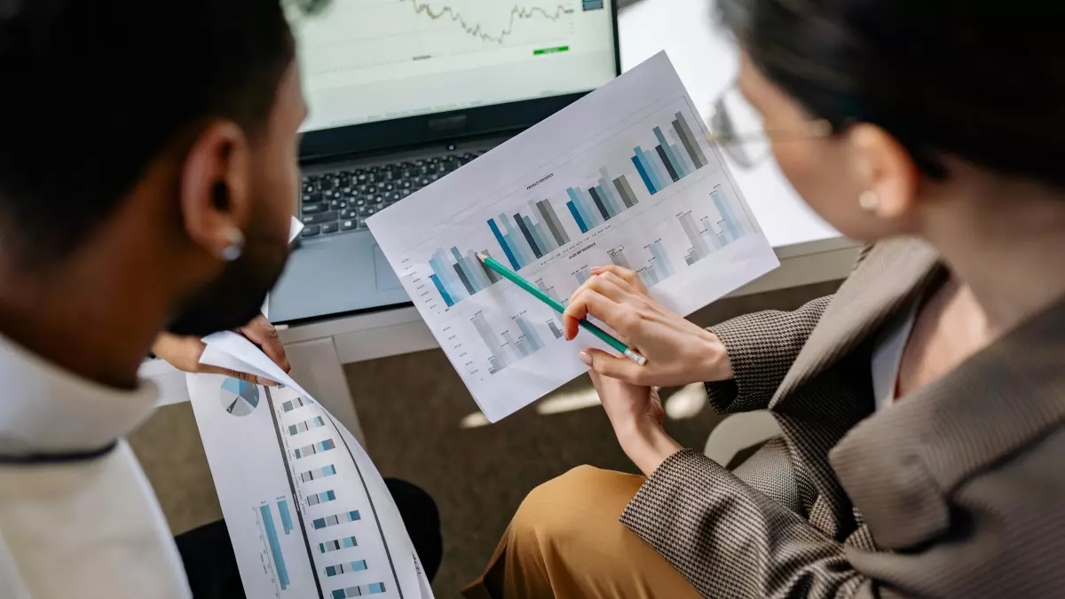 Two people analyzing data on paper and a laptop in an office setting.