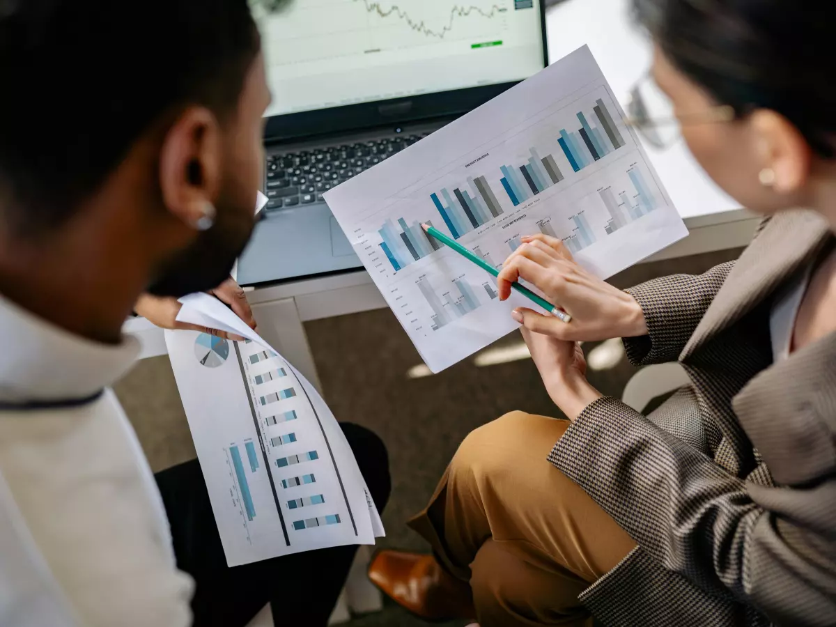 Two people analyzing data on paper and a laptop in an office setting.