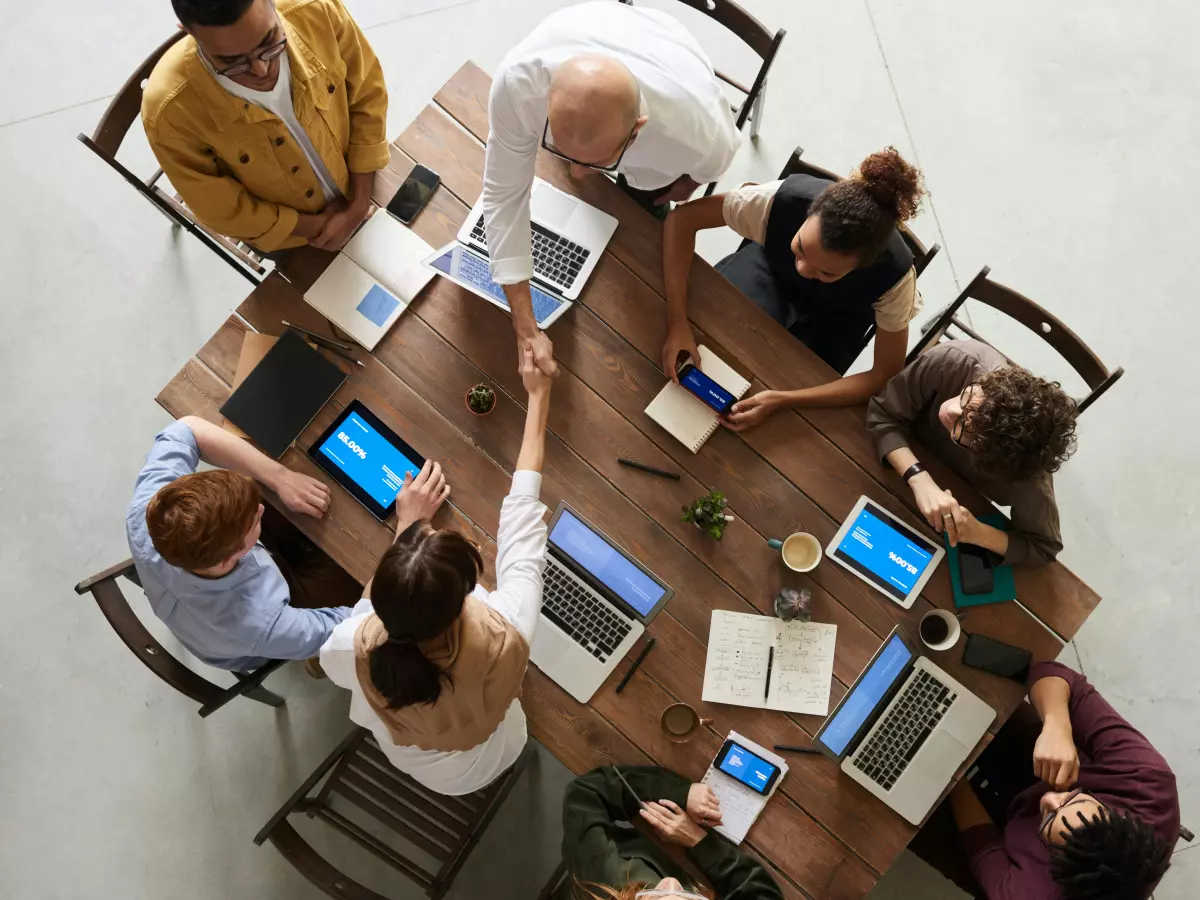 A group of people are sitting around a table in a meeting room, discussing business. The scene is energetic and lively. 