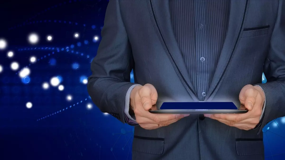 A person in a suit holds a tablet in front of a blue background with abstract network connections and white dots.