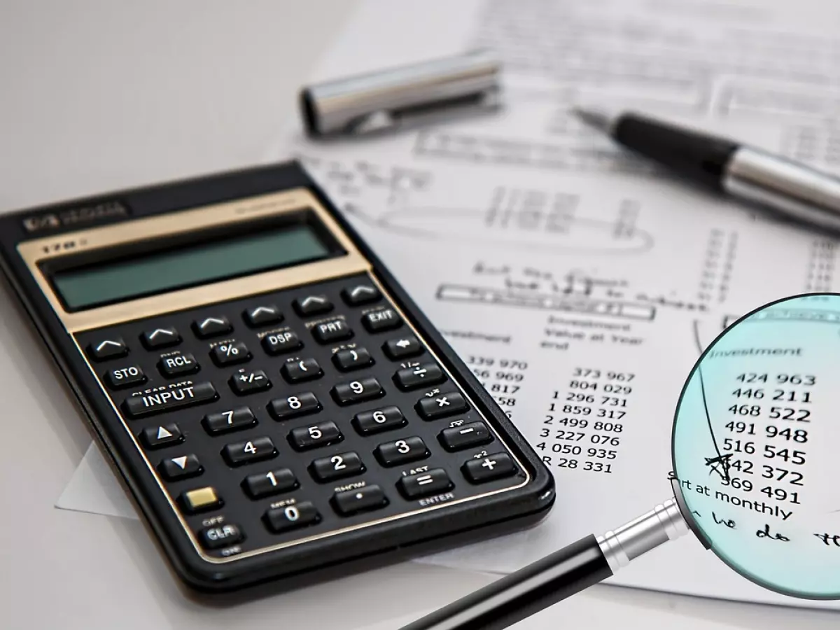 A calculator, magnifying glass, and financial documents on a table.