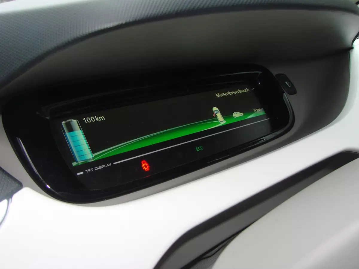 A close-up of an electric car's dashboard showing a digital display with a range of 100km.