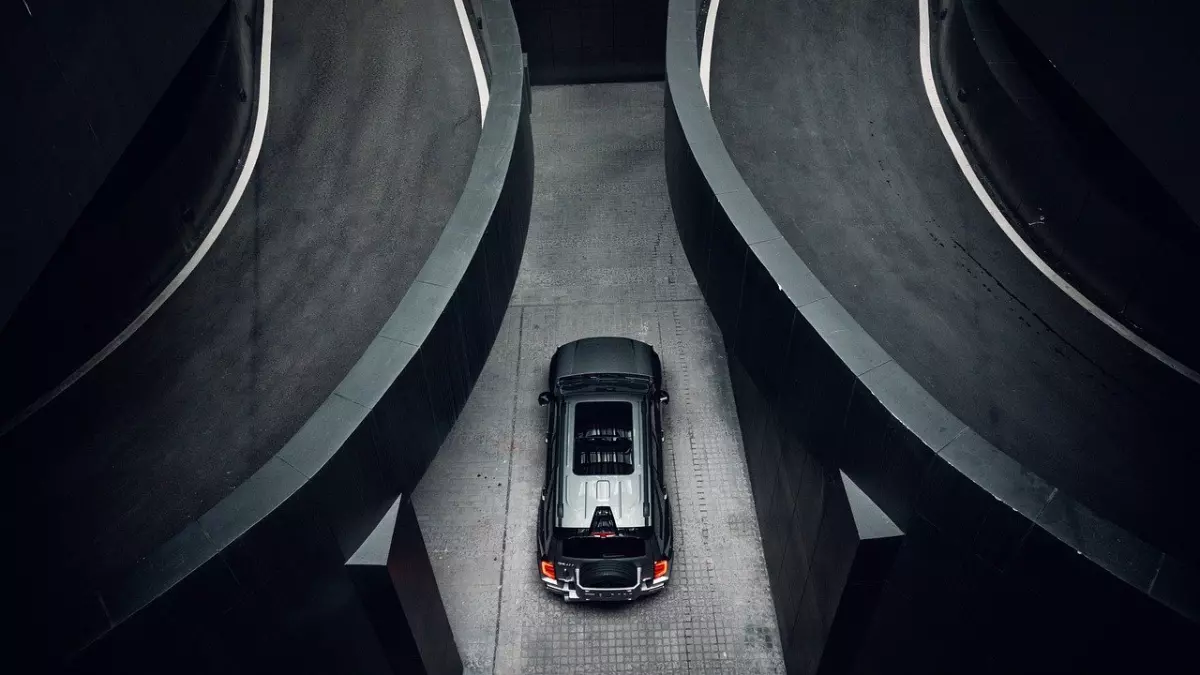 A silver Volvo EX90 SUV is parked in a concrete parking garage. The car is seen from above, and the image is composed in a way that emphasizes the car