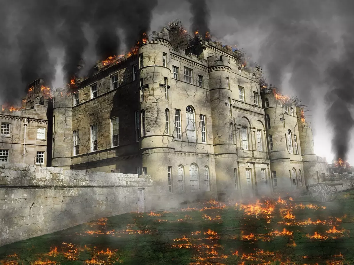 A large castle is engulfed in flames. There's smoke billowing from the top. The castle is surrounded by a wall with a gate.