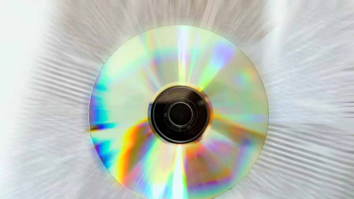 A close-up image of a CD, with light shining through it. The image is taken at a low angle, creating a sense of depth and perspective. The CD is in focus, while the background is blurred.