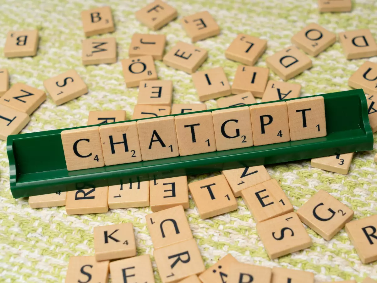 The word 'CHATGPT' spelled out using Scrabble tiles, with other tiles scattered around.