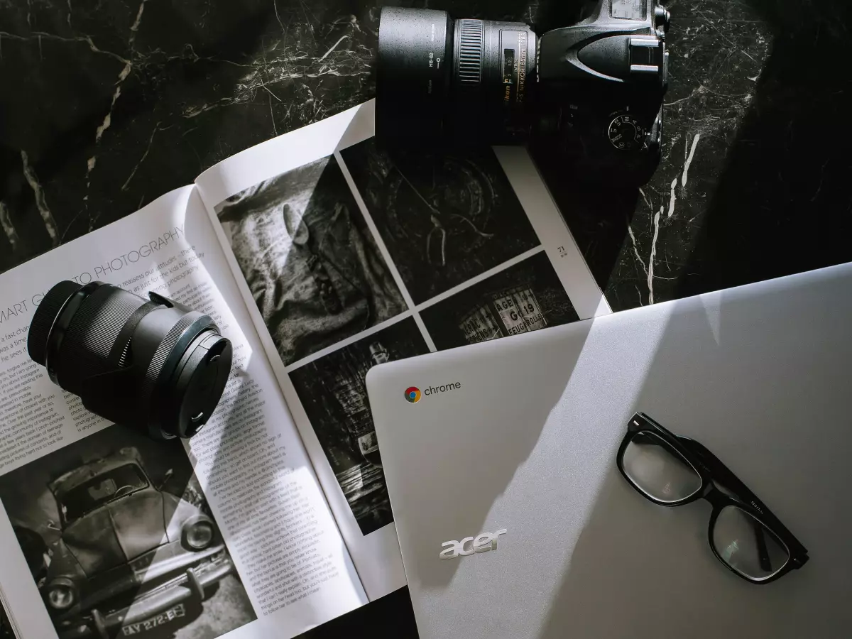 A silver Acer laptop with a detachable controller, next to a camera and magazine.