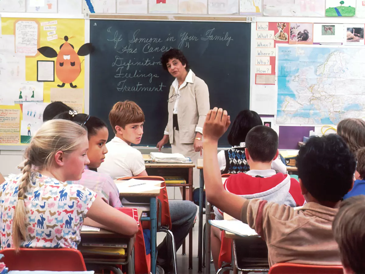 A classroom setting with a teacher and students, featuring technology use.