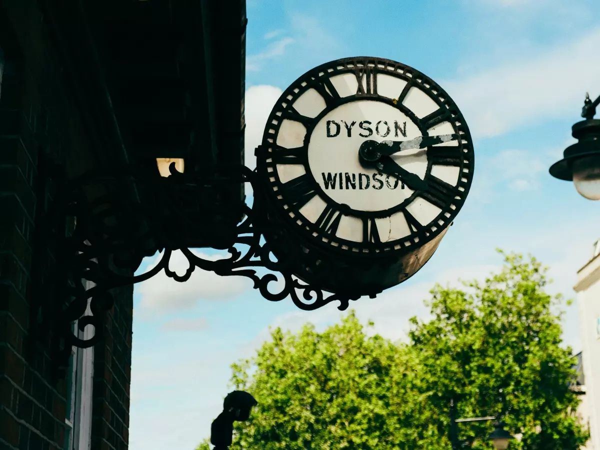 A close-up of a large clock with the words "Dyson Windsor" on the face. The clock is mounted on the side of a building.