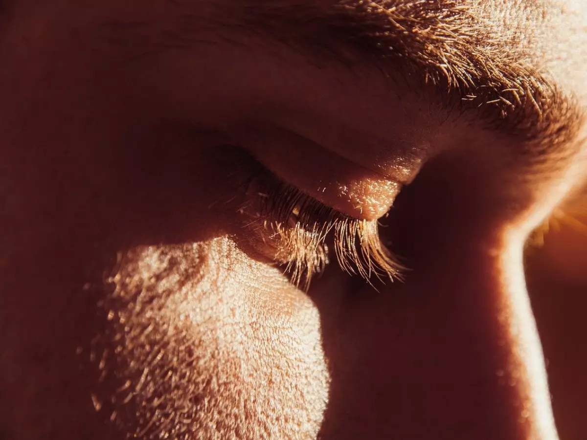 Close-up of a man's eye closed with eyelashes in focus. Sunlight hits the face.