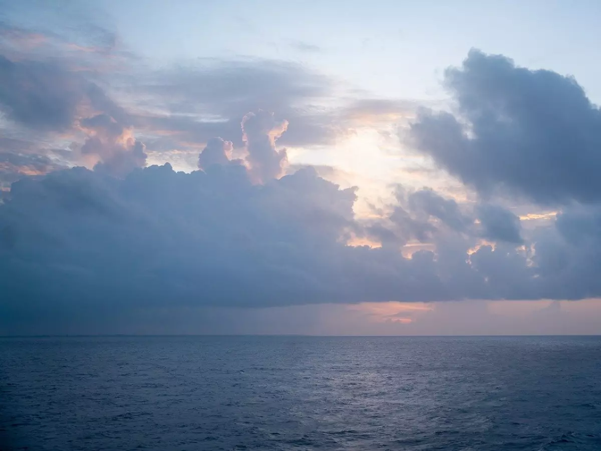 A stormy sky over the ocean with the sun peeking through the clouds.