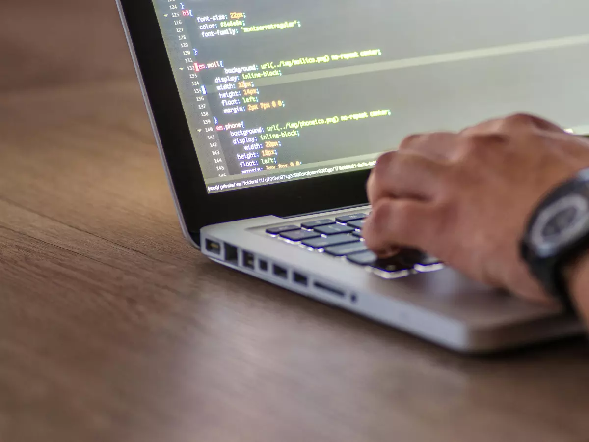 A person's hands typing on a laptop keyboard with code visible on the screen.