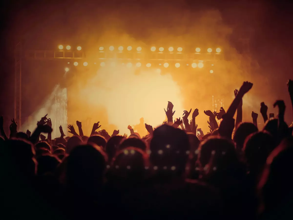 A large crowd of people with their hands in the air in front of a stage with bright lights.