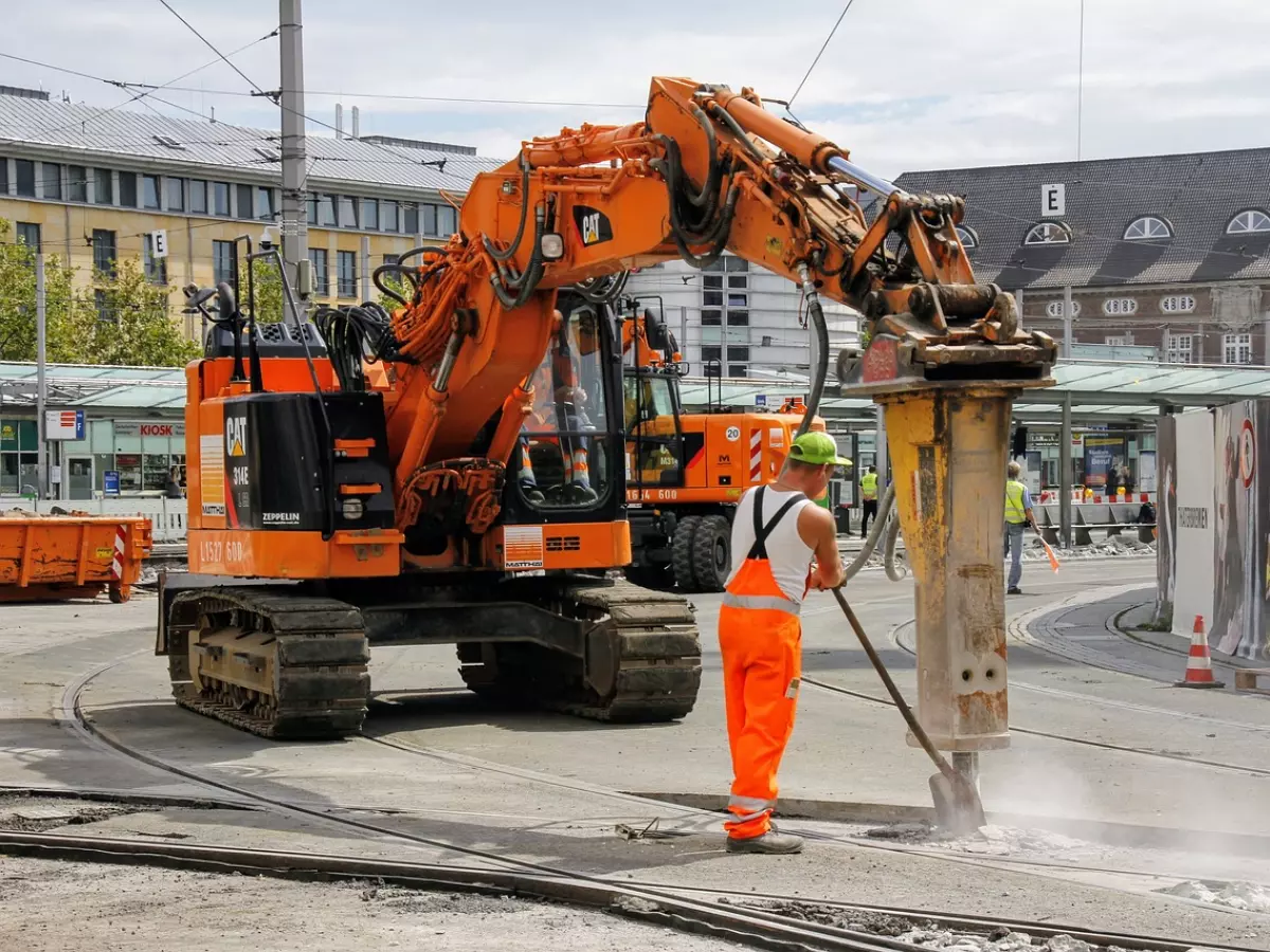 Construction worker using a jackhammer with a large construction vehicle in the background