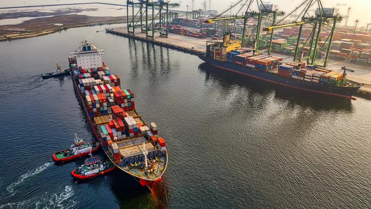 Aerial view of a large container ship being assisted by tugboats in a harbor.