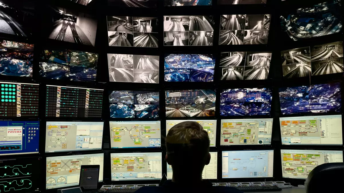 A person sits in front of a wall of monitors, each displaying surveillance footage.