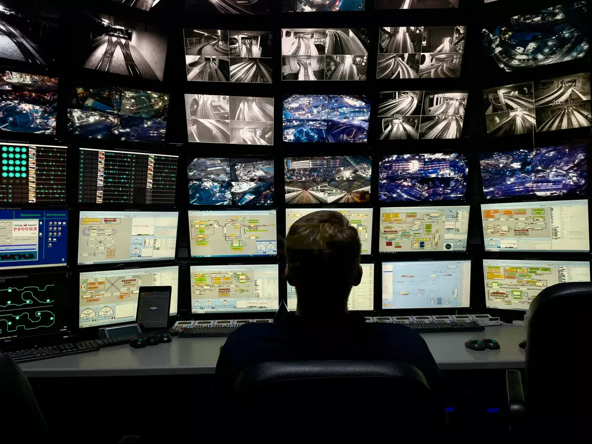 A person sits in front of a wall of monitors, each displaying surveillance footage.