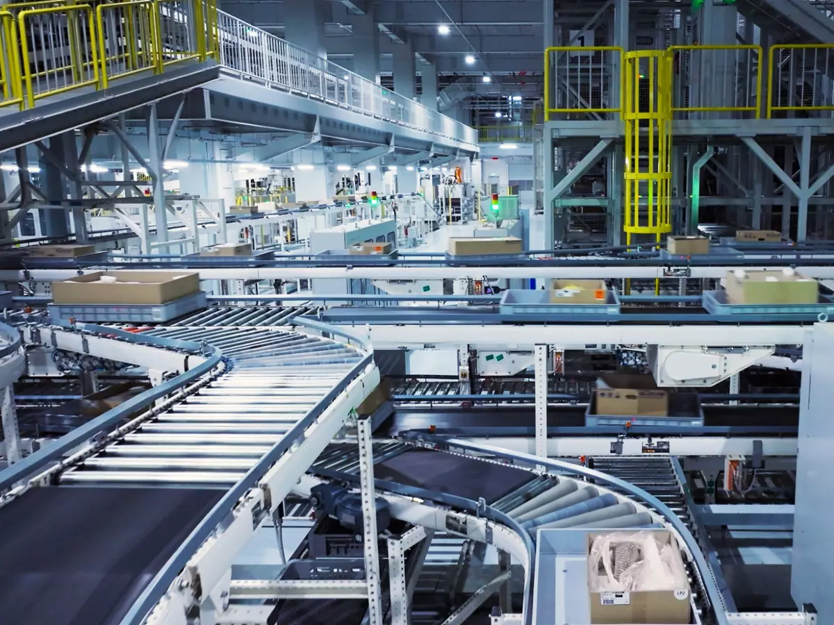 A conveyor belt system in an industrial factory. The belts are moving and carrying boxes. The factory is well-lit and has a lot of metalwork.