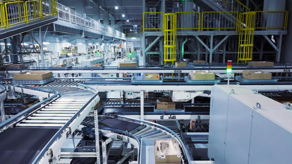 A conveyor belt system in an industrial factory. The belts are moving and carrying boxes. The factory is well-lit and has a lot of metalwork.