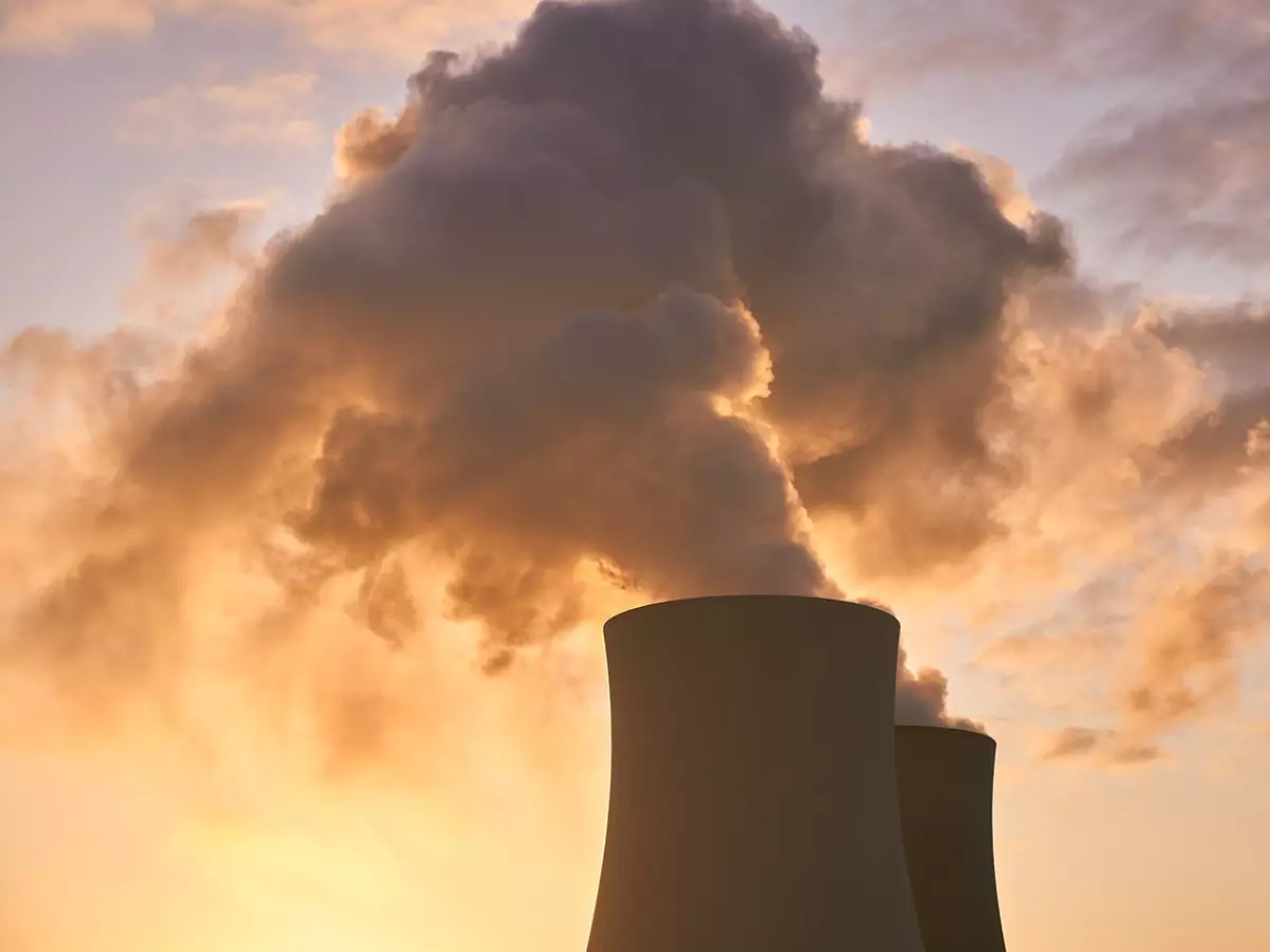 A nuclear power plant with two large cooling towers, the towers are emitting smoke against a sunset sky. 