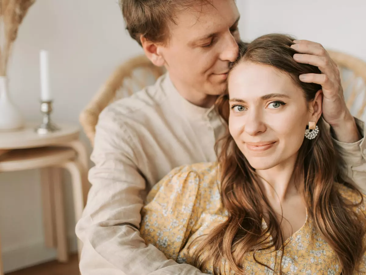 A couple sitting on a chair, the man is touching the woman's hair.