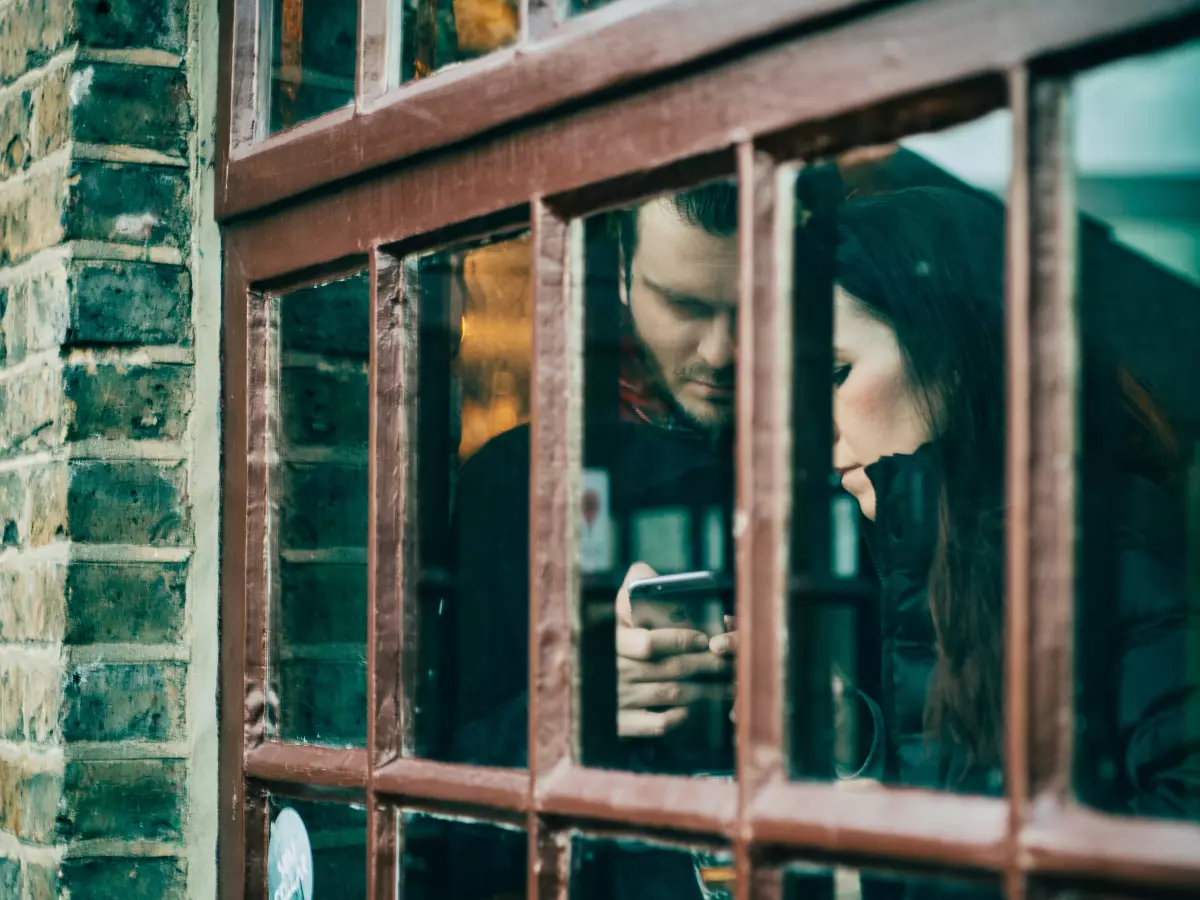 Two people are looking at a smartphone through a window, suggesting communication or messaging.