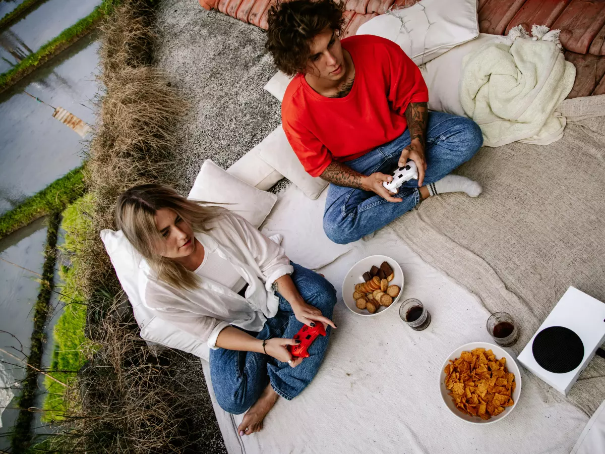 Two people playing on a white Xbox console outdoors.