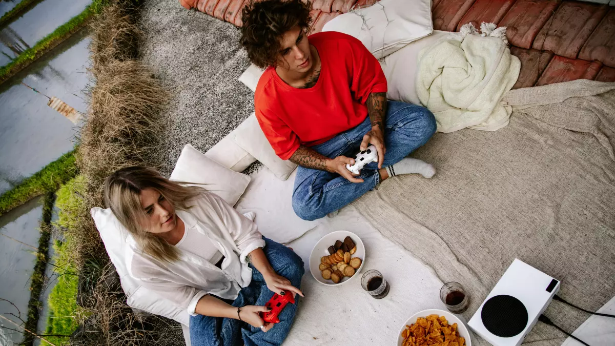 Two people playing on a white Xbox console outdoors.