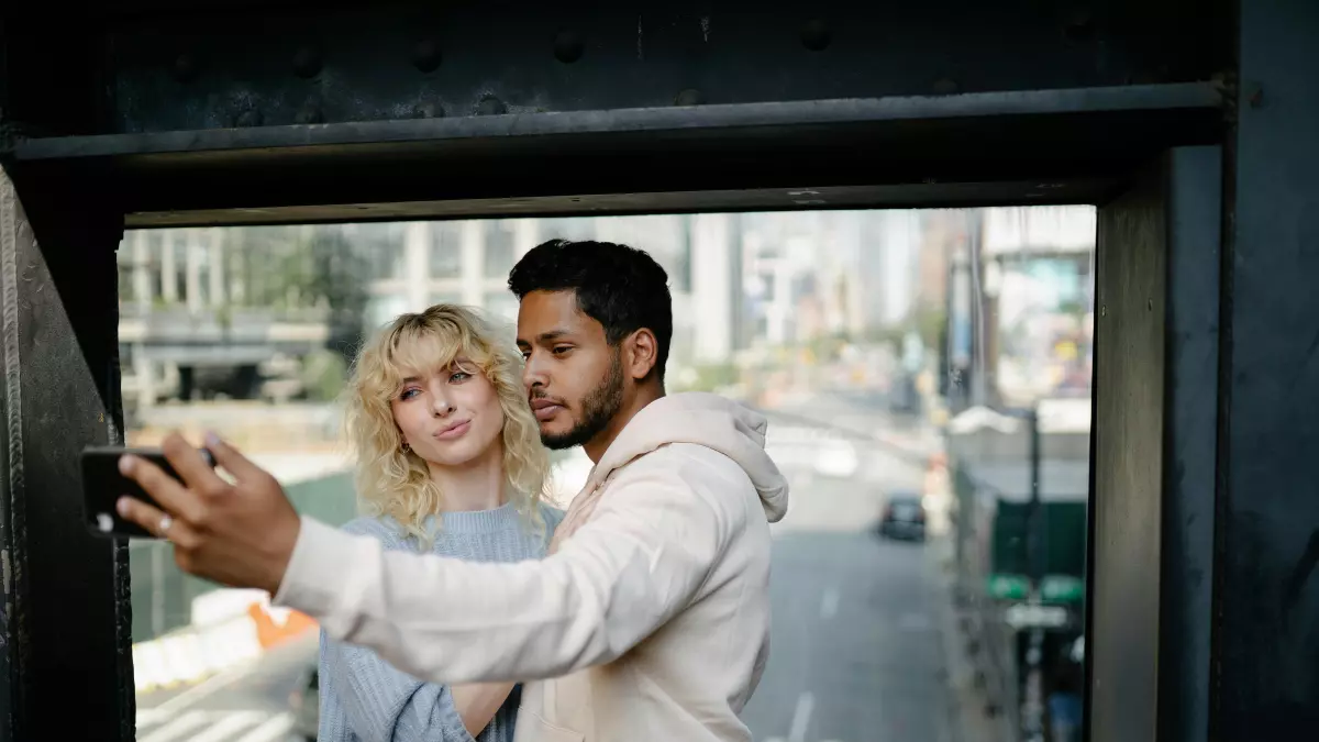 A couple taking a selfie with a phone in front of a cityscape.