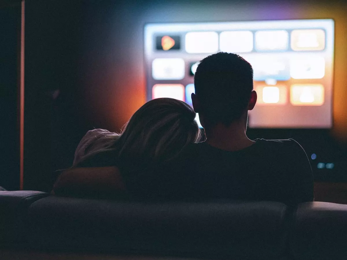 A couple is watching television. The screen is lit up with a bright white light and shows a variety of content options.