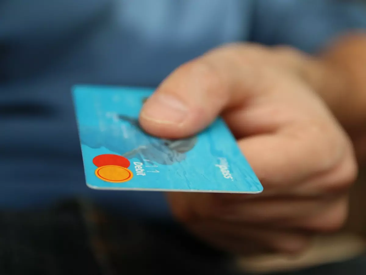 A person's hand holding a blue credit card with the word 'Debit' on it.