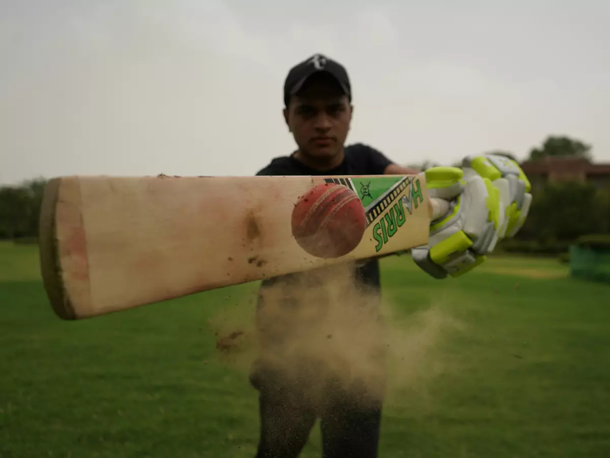 A man is playing cricket with a bat hitting the ball.