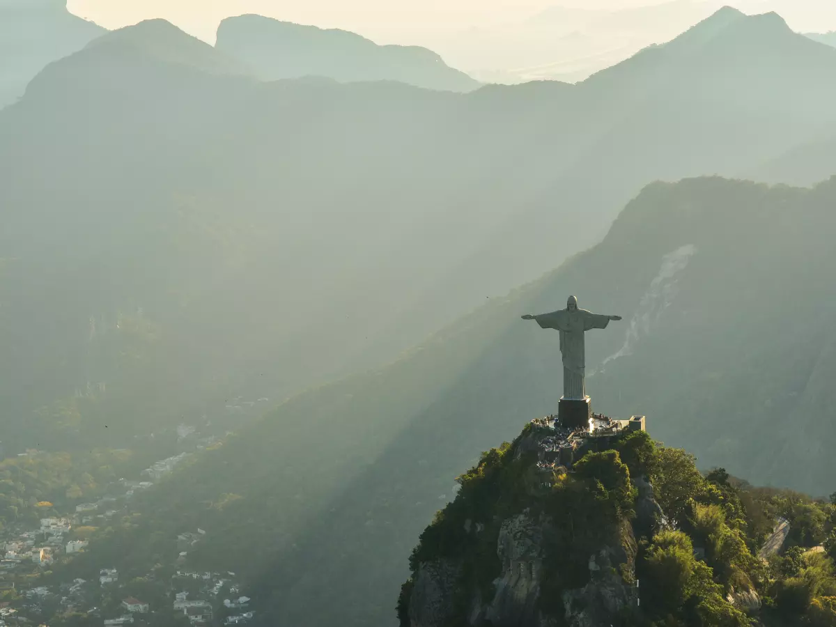 A panoramic view of Rio de Janeiro, Brazil, showcasing the iconic Christ the Redeemer statue atop Corcovado Mountain, with the sprawling cityscape and lush greenery in the foreground.