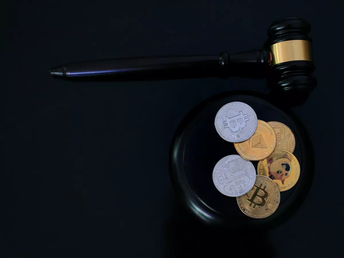 A gavel sits on a black surface, surrounded by several crypto coins, including Bitcoin, Ethereum, and others. The image has a dark and ominous tone.