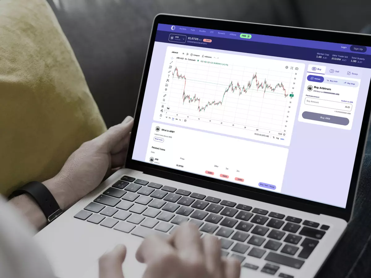 A person sitting on a couch using a laptop with a cryptocurrency graph displayed on the screen