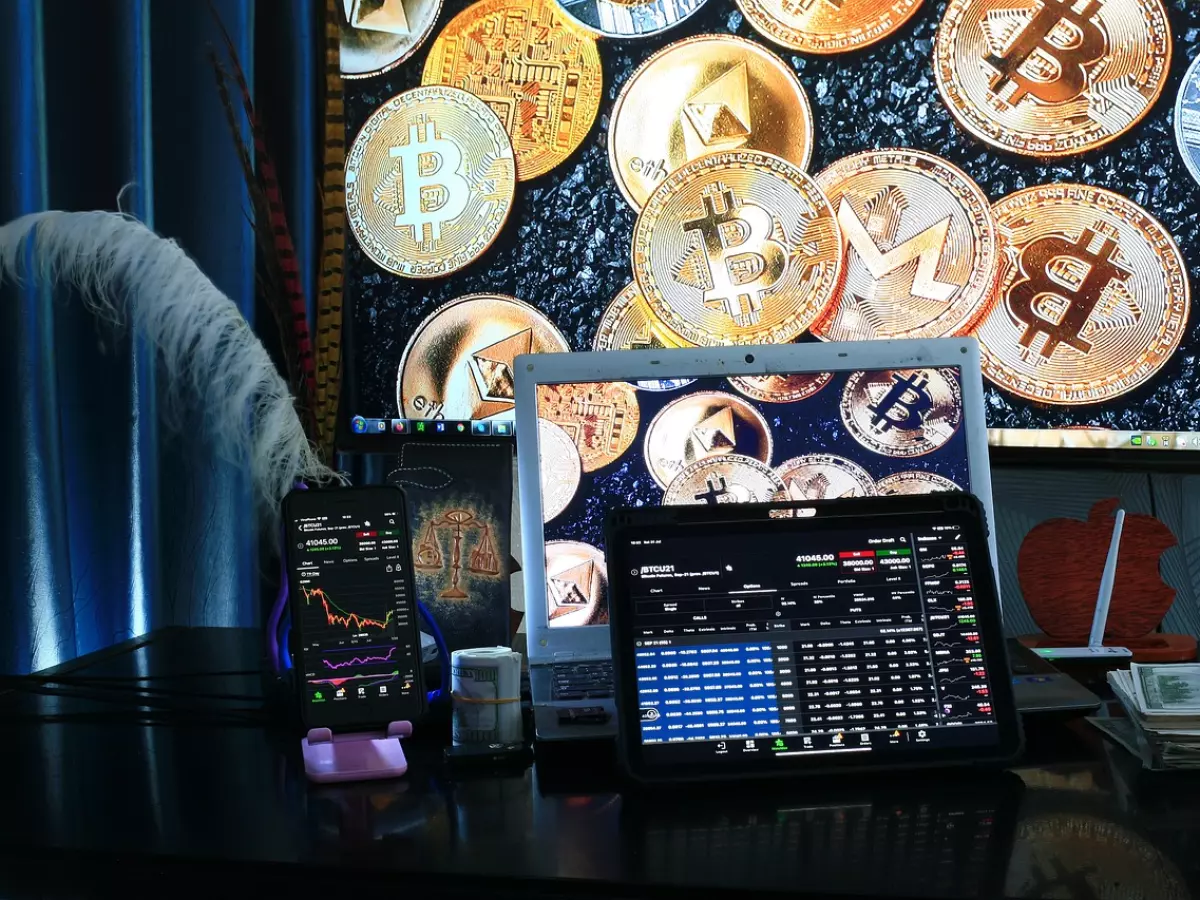 A desk with a laptop, tablet, smartphone, and cash, with a Bitcoin background on the laptop screen.