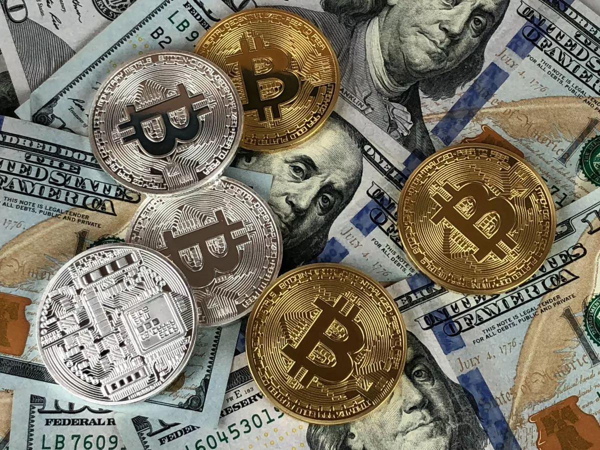 Close-up shot of Bitcoin coins on top of US dollar bills, highlighting the connection between cryptocurrency and traditional finance.