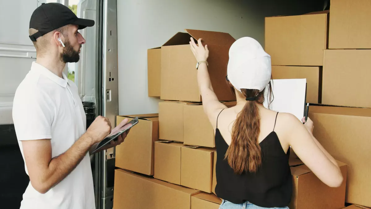 A man and a woman checking boxes inside a delivery truck.