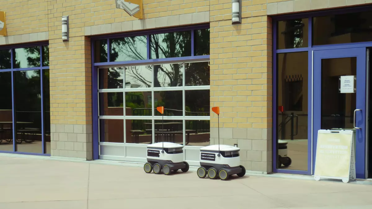 Two small autonomous robots with sensors on top of them, parked in front of a building.