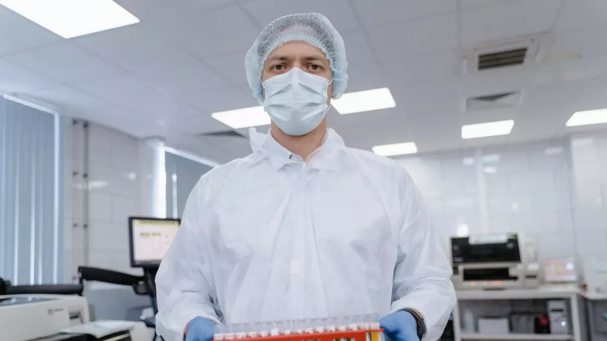 A scientist in a lab setting holds a tray of test tubes, looking directly at the camera.