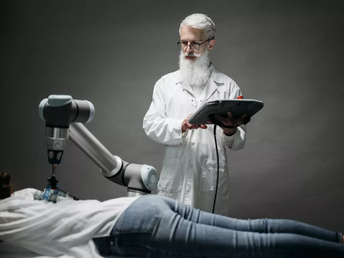 A doctor in a white coat stands next to a patient who is laying on a table while a robotic arm moves near the patient.