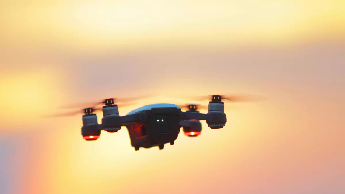 A black drone flies in the sky against a dramatic sunset background.