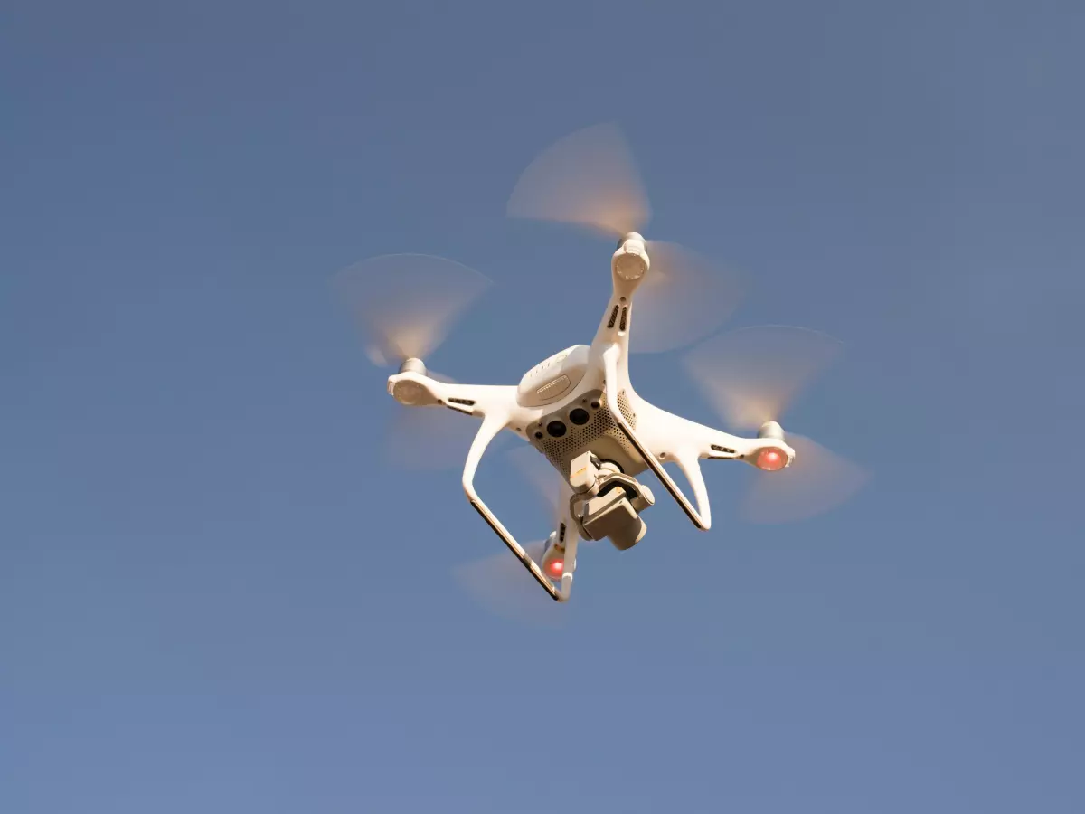 A white drone flying in the air with its propellers spinning.