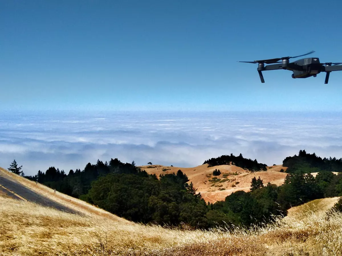 A drone flying in the sky above a field of grass and trees