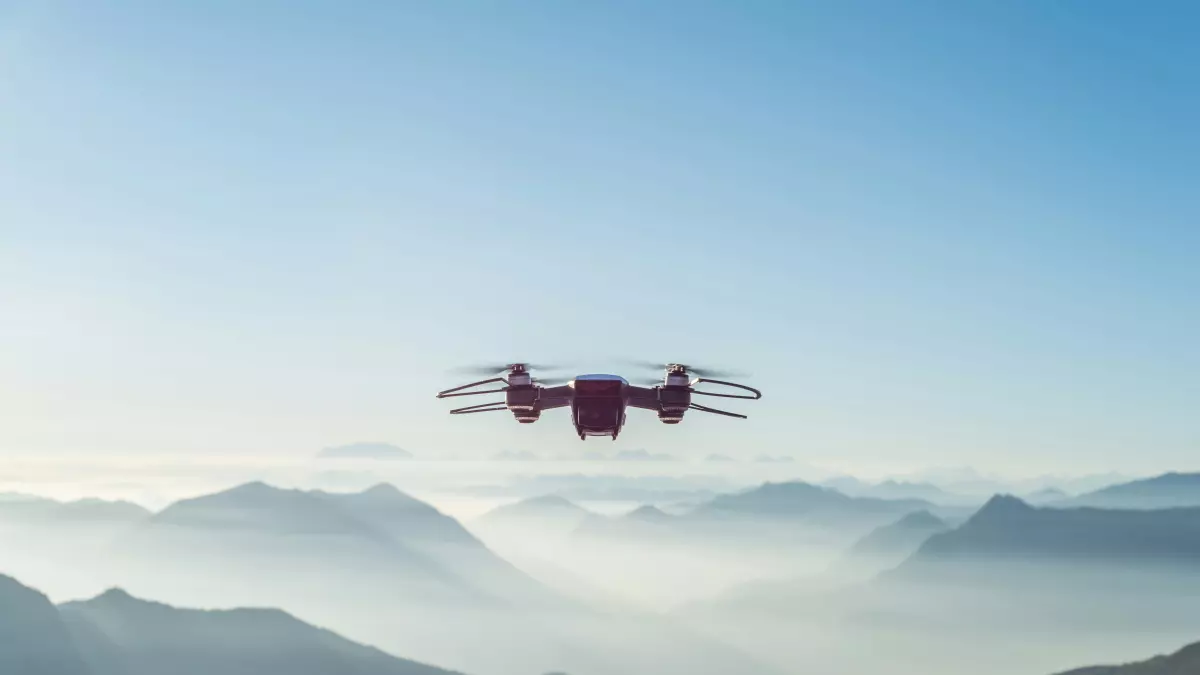 A red drone flying over mountains.