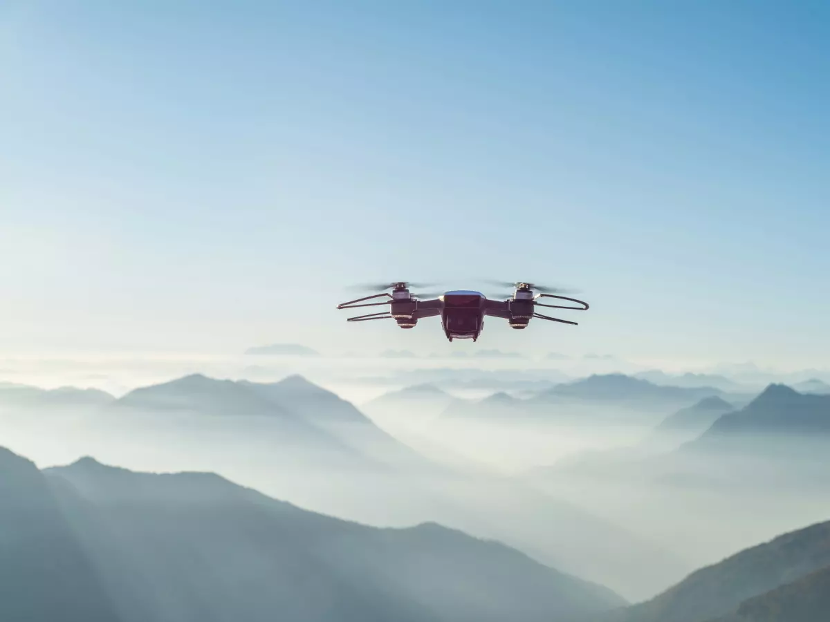 A red drone flying over mountains.