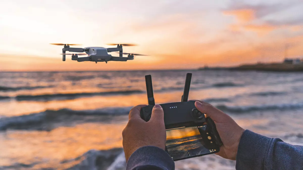 Person holding drone remote control with a drone flying in the air