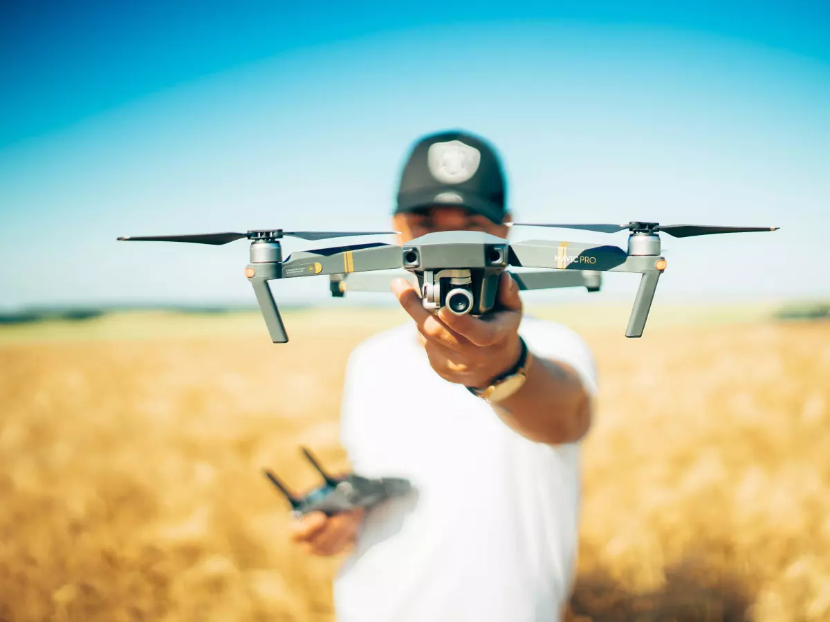 A drone flying over a field of tall grass. The sky is blue and the grass is a light yellow.